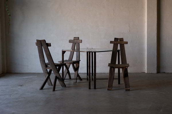 Front angle of triangular glass-top side tables with iron frames surrounded by wooden lounge chairs.