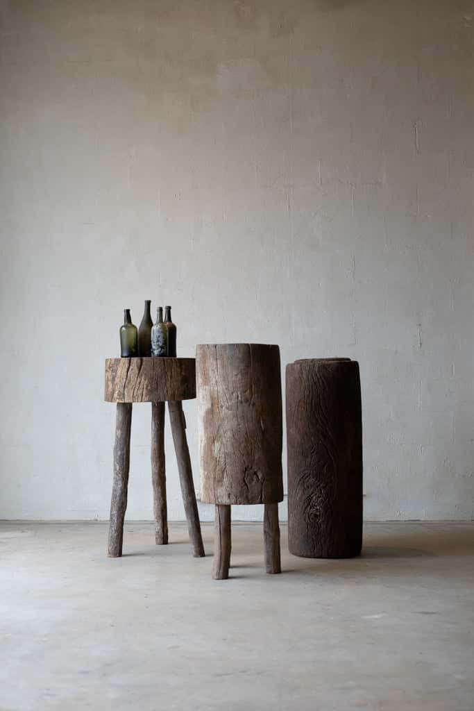 Three tree-trunk tables in French butcher block style: one is a small cylinder with three wood peg legs; one is a long block of trunk with three short legs; one is a tall section of tree trunk. 