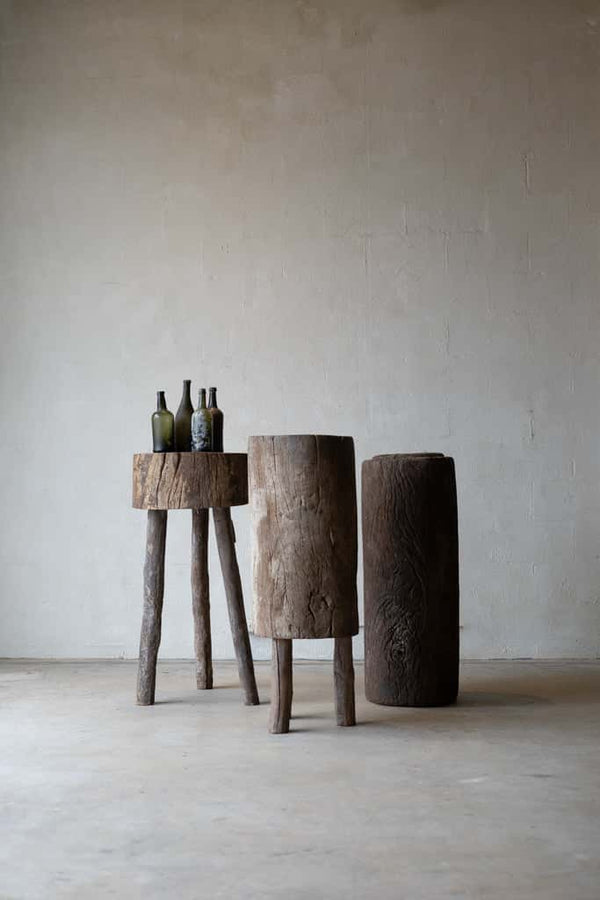 Three tree-trunk tables in French butcher block style: one is a small cylinder with three wood peg legs; one is a long block of trunk with three short legs; one is a tall section of tree trunk. 