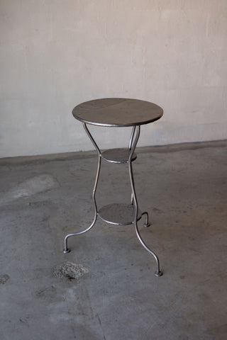 Front angled view of iron side table, showing circular top, curved legs, and welded joints.