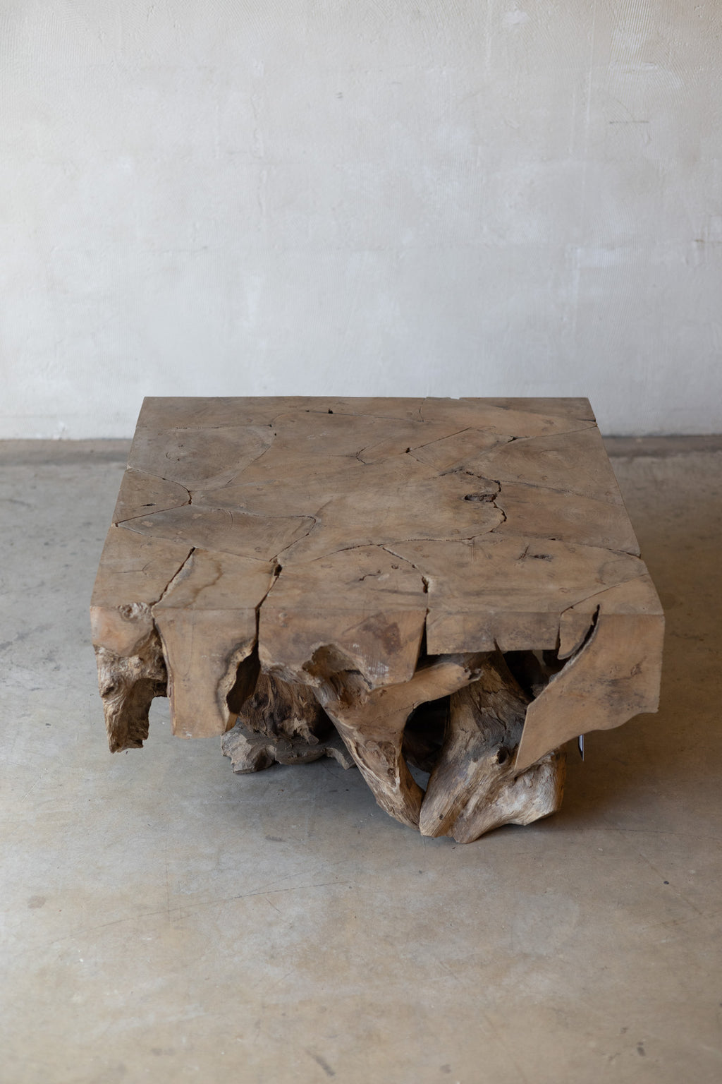 A rustic square wooden coffee table made from a natural live-edge wood slab, set against a neutral concrete wall and floor.
