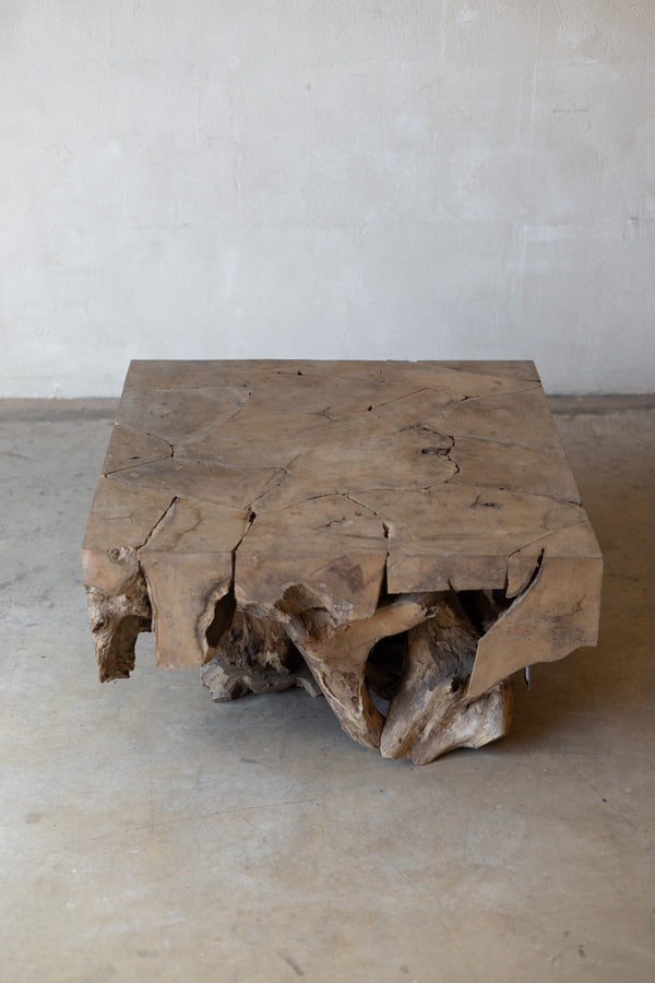 A rustic square wooden coffee table made from a natural live-edge wood slab, set against a neutral concrete wall and floor.