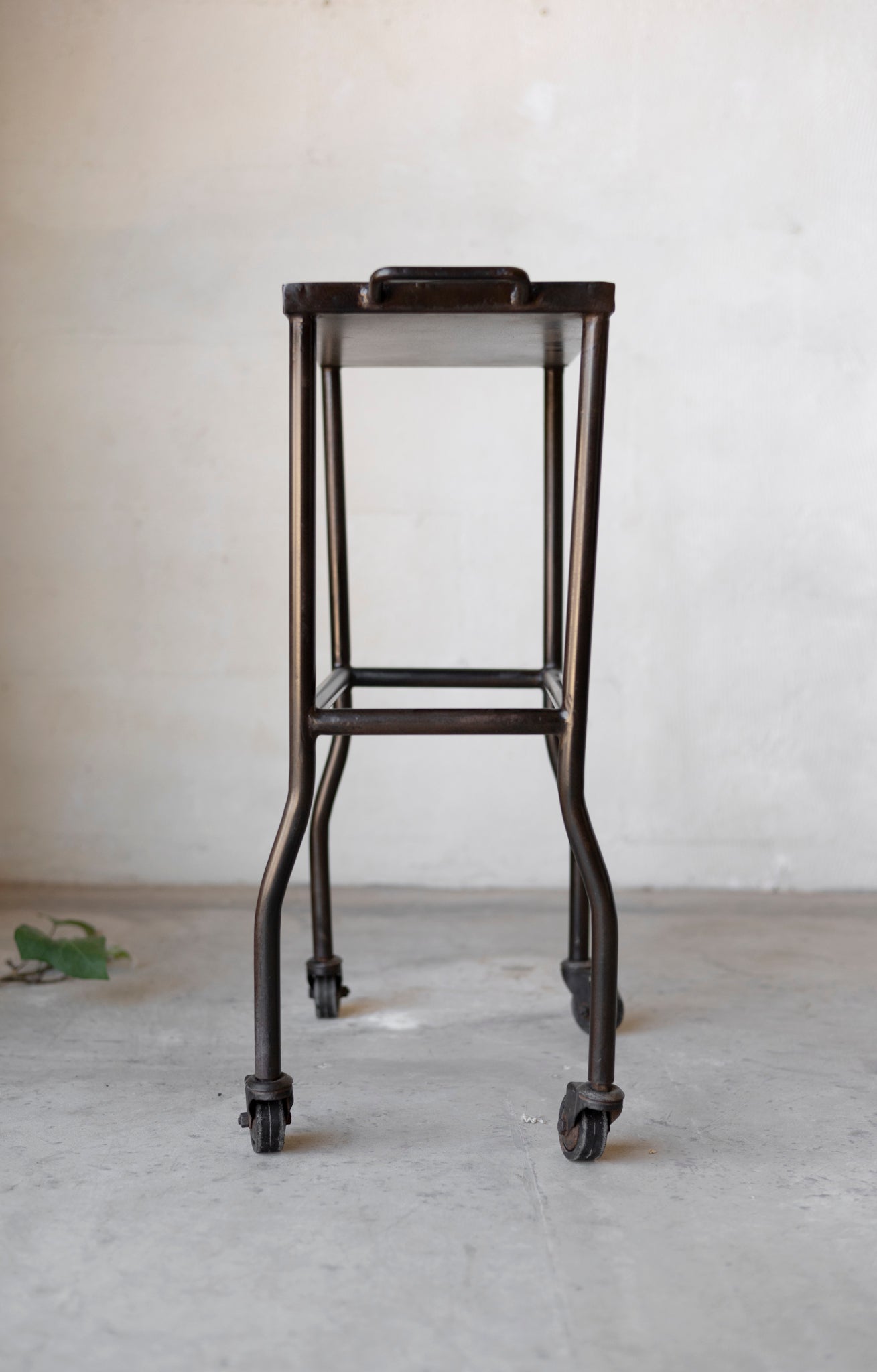 Black metal bar stool with wheels on a plain background