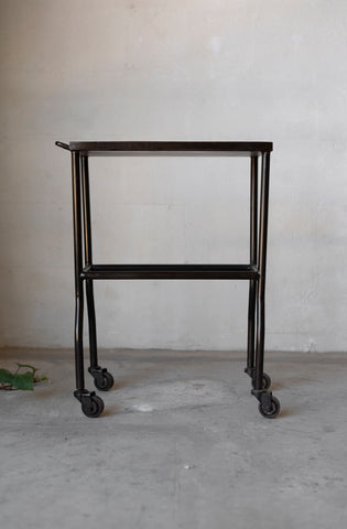 Black metal side table with wheels on a gray floor against a plain wall