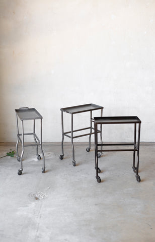 Three metal bar stools on wheels against a plain white wall.