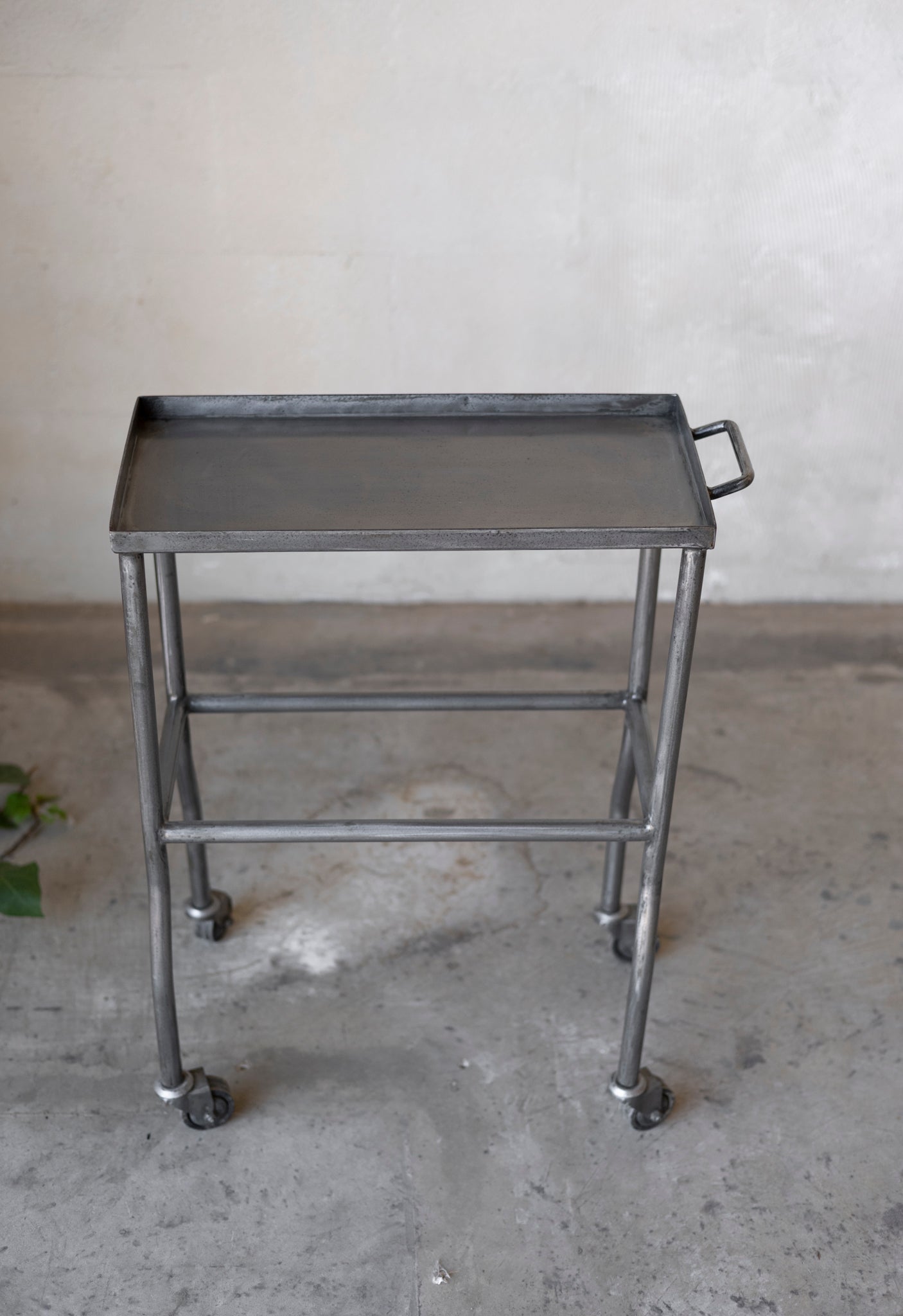 Metal rolling table with a tray on a concrete floor.