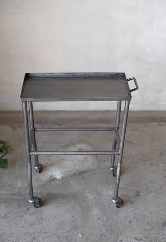Metal rolling table with a tray on a concrete floor.