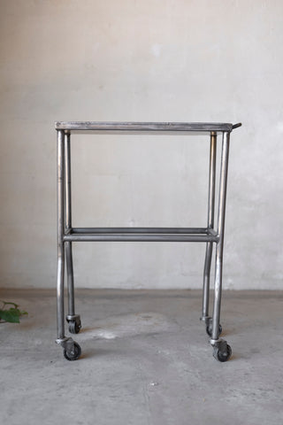 Metal rolling cart on wheels against a plain wall.