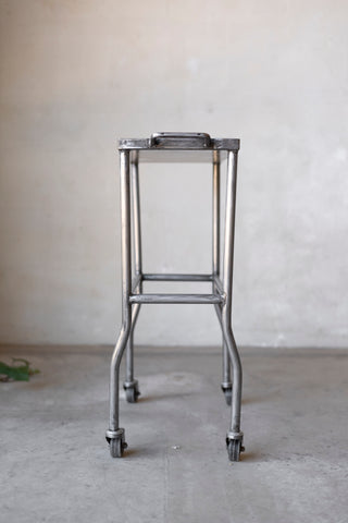 Metal stand with wheels on a concrete floor against a plain wall