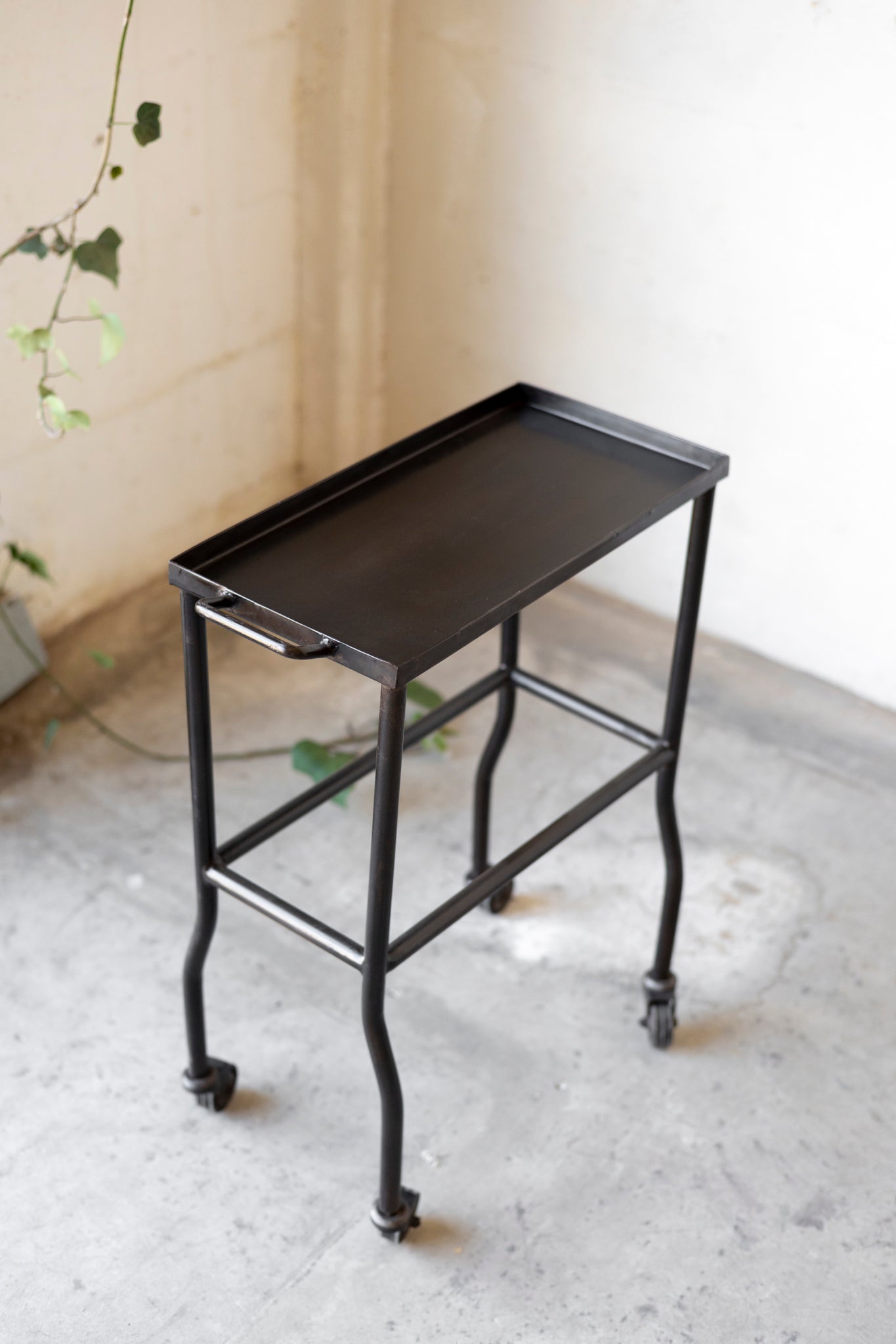 Black metal side table with wheels on a light gray floor.