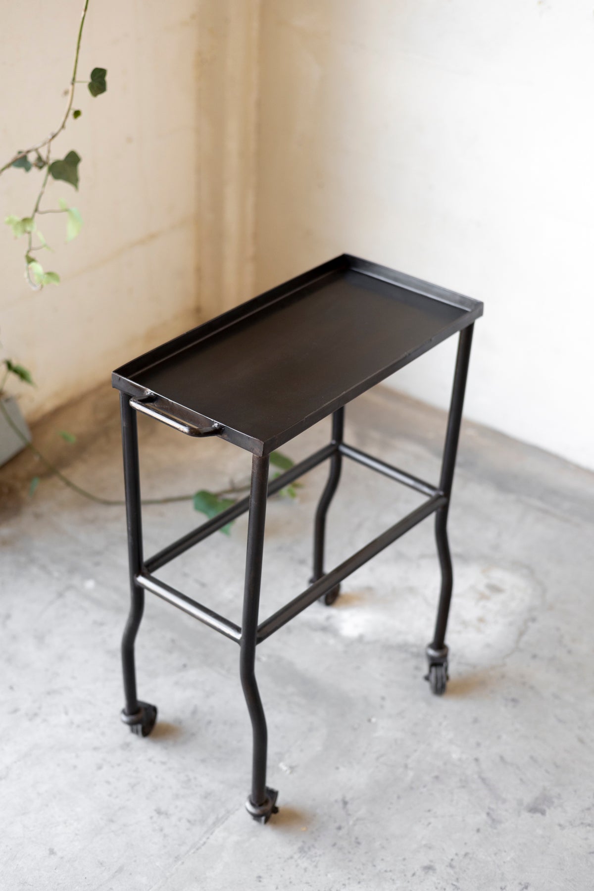 Black metal side table with wheels on a light gray floor.