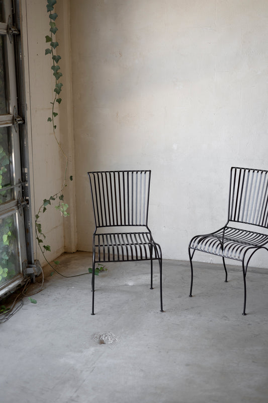 Two black metal chairs in a room with a textured wall and concrete floor.