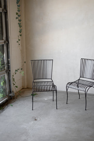 Two black metal chairs in a room with a textured wall and concrete floor.
