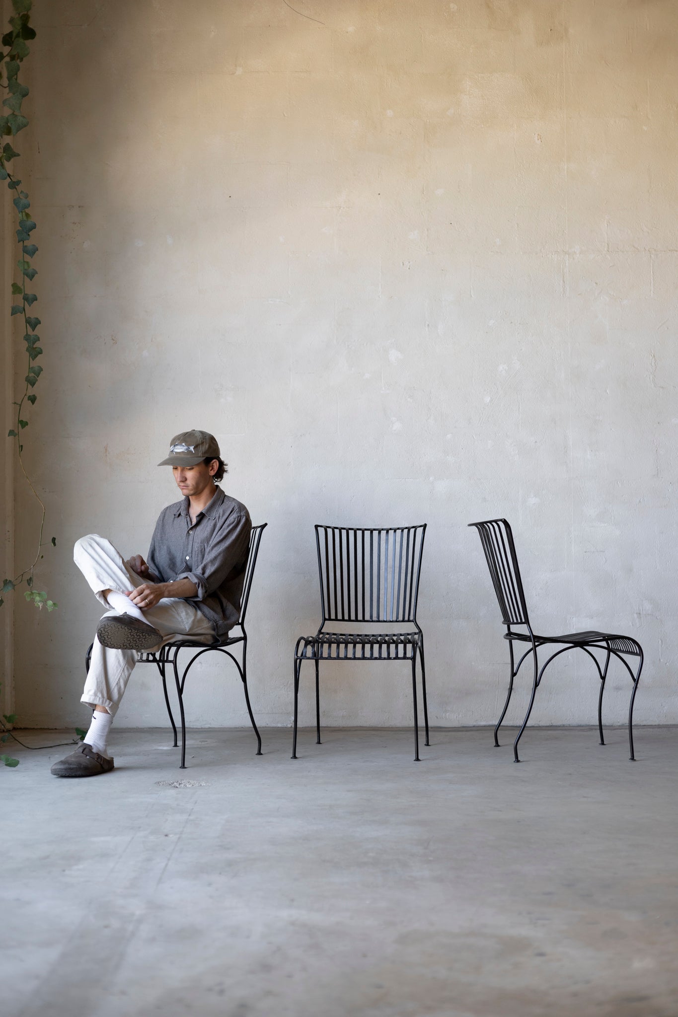 Person sitting on a chair reading a newspaper with two additional chairs in a minimalistic room.