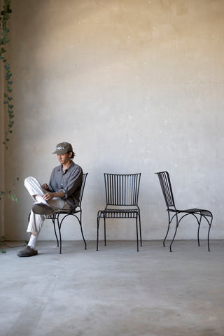 Person sitting on a chair reading a newspaper with two additional chairs in a minimalistic room.