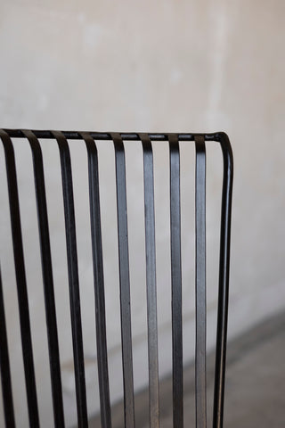 Close up of the corner of a black iron slatted chair against a blurred white background.