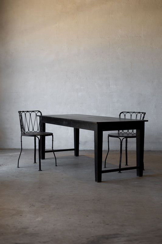 Black table with two matching chairs against a plain wall.