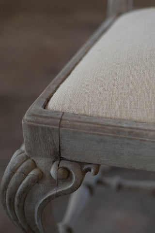 Close-up of a chair with detailed wooden frame and beige cushioned seat.