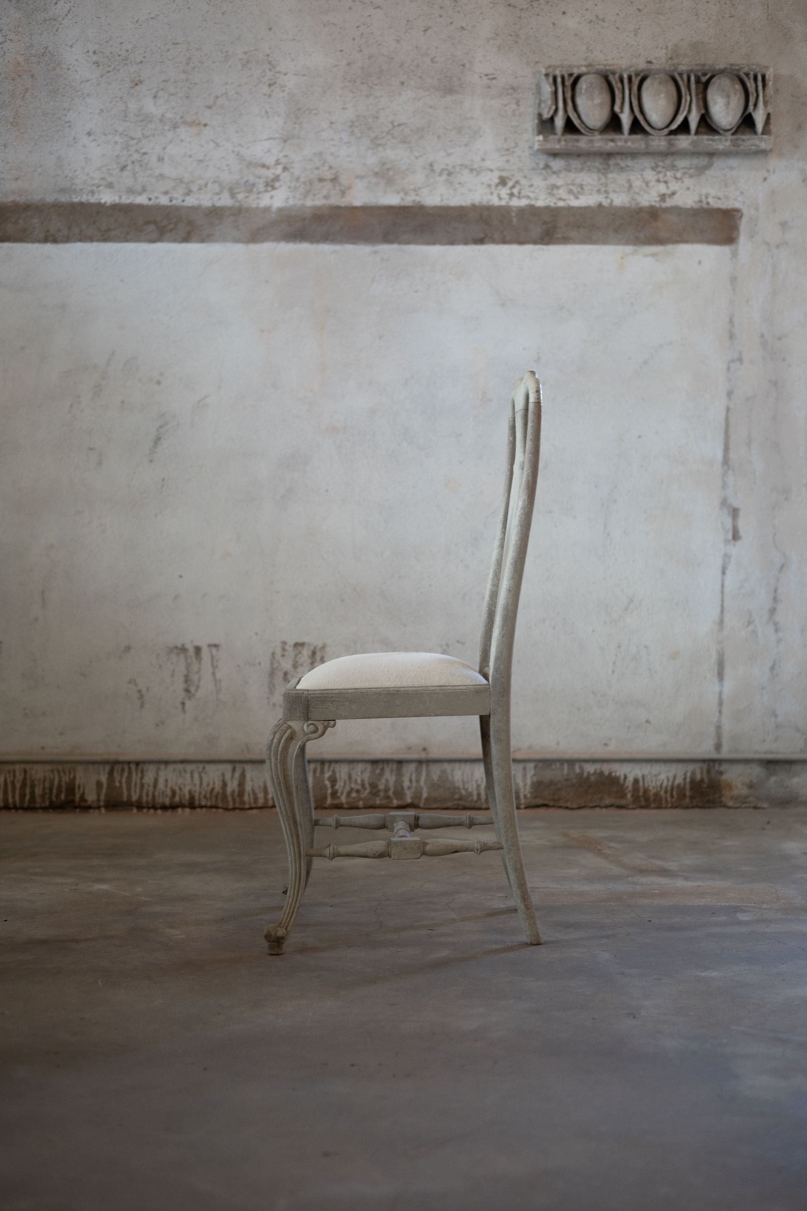 Side of white chair in a room with a textured wall and concrete floor