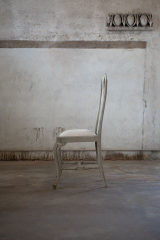 Side of white chair in a room with a textured wall and concrete floor