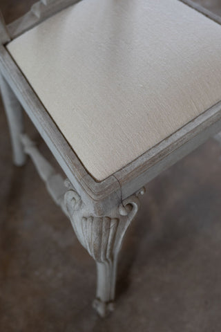 Close-up of a decorative chair with a beige cushioned seat on a wooden floor.