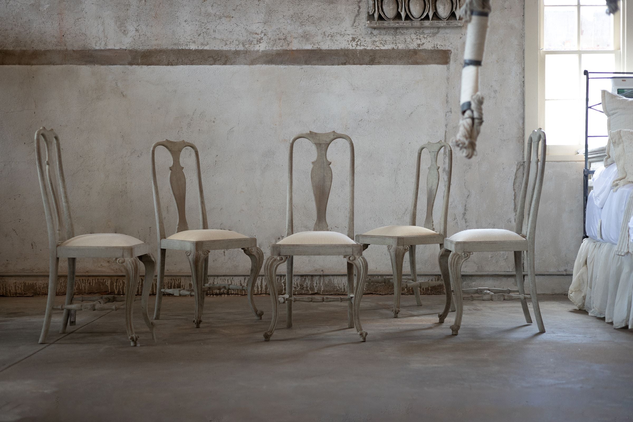 Set of five vintage-style chairs in a room with textured walls and a bed in the background.