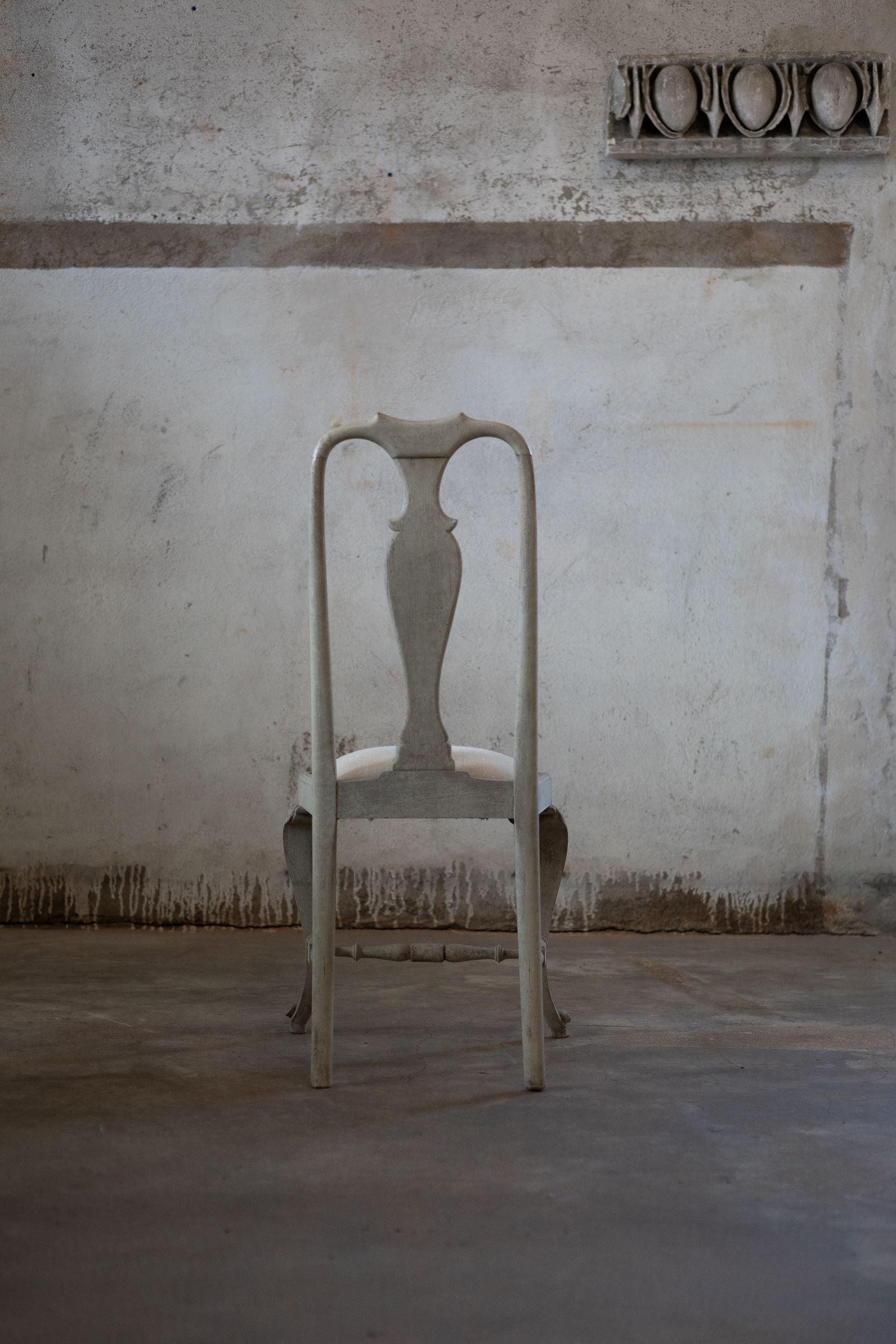 Vintage wooden dining chair in a room with a textured wall and concrete floor.