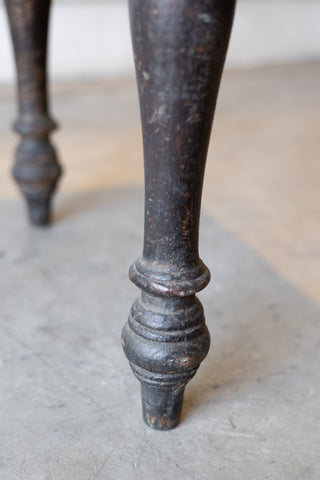 Close up of leg of vintage colonial teak wood desk with turned legs against a plain background.