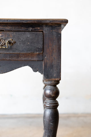 Close up of corner of vintage colonial teak wood desk showcasing wear and patina against a plain background.