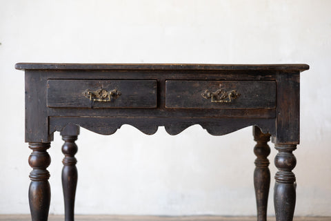 Vintage colonial teak wood desk with two drawers against a white wall.