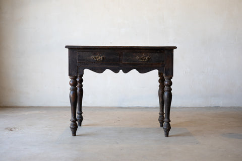 Vintage colonial teak wood desk with turned legs against a plain background.