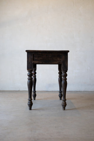 Side view of vintage colonial teak wood desk with turned legs against a plain background.