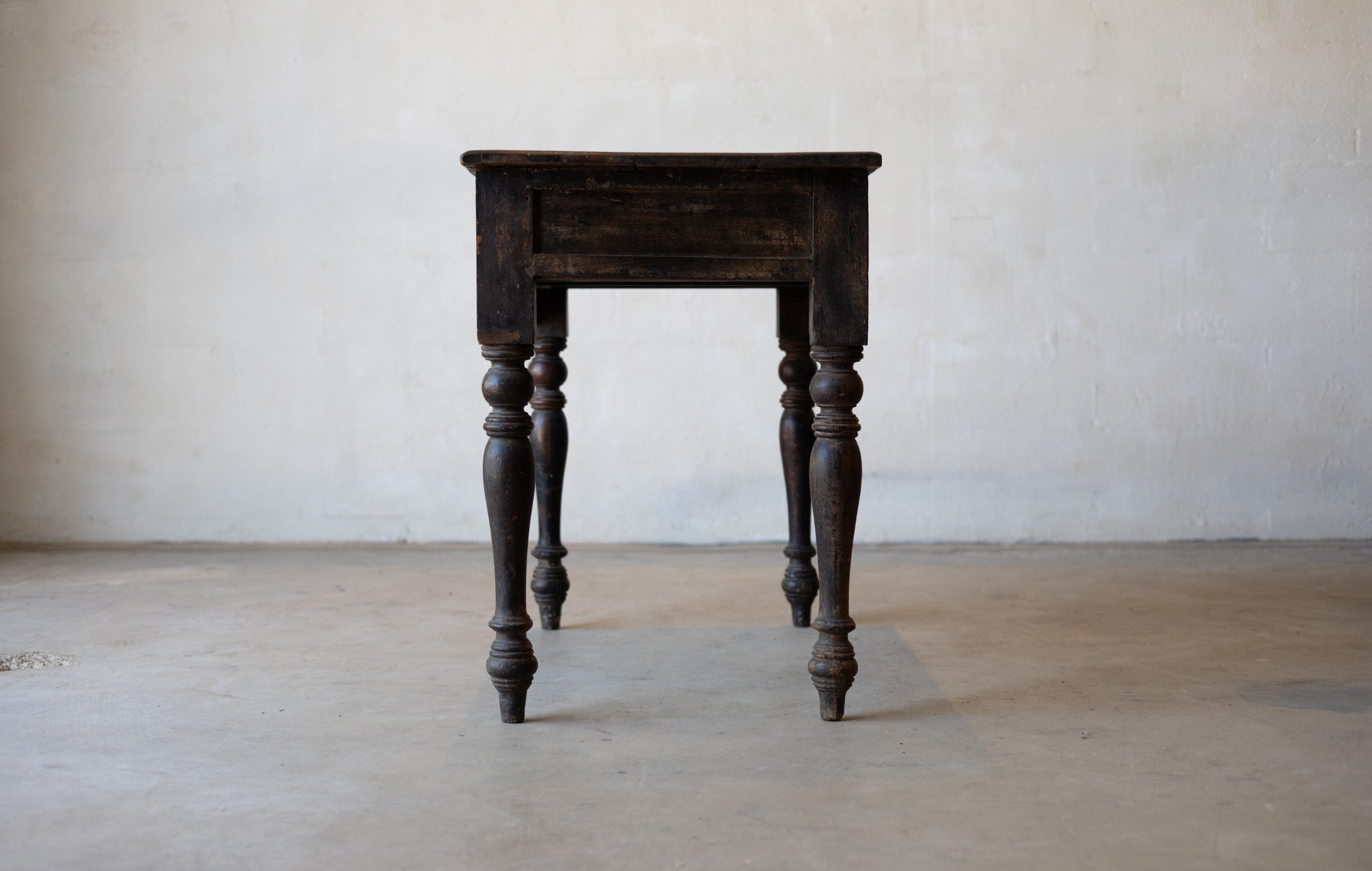 Side of vintage colonial teak wood desk with turned legs against a plain background.