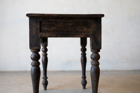 Close up of side of vintage colonial teak wood desk with turned legs against a plain background.