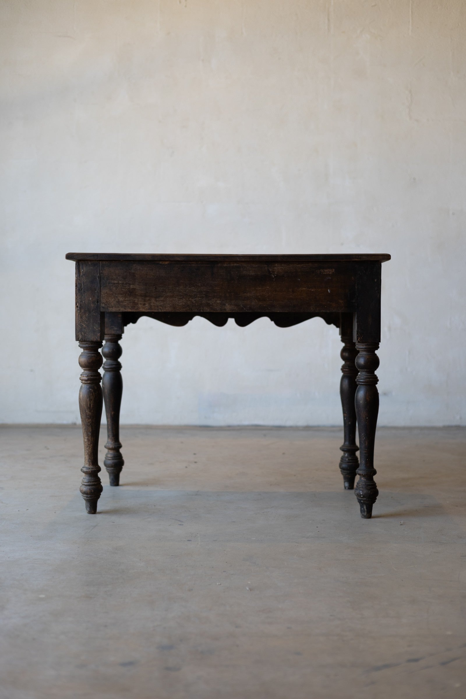back of vintage colonial teak wood desk with turned legs against a plain background.
