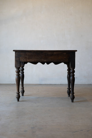 back of vintage colonial teak wood desk with turned legs against a plain background.