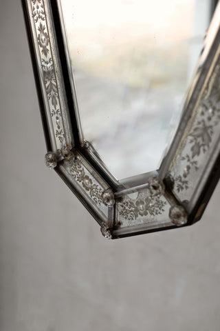 Close-up of an antique Venetian mirror with a beveled glass frame adorned with intricate floral etchings and decorative glass rosettes.
