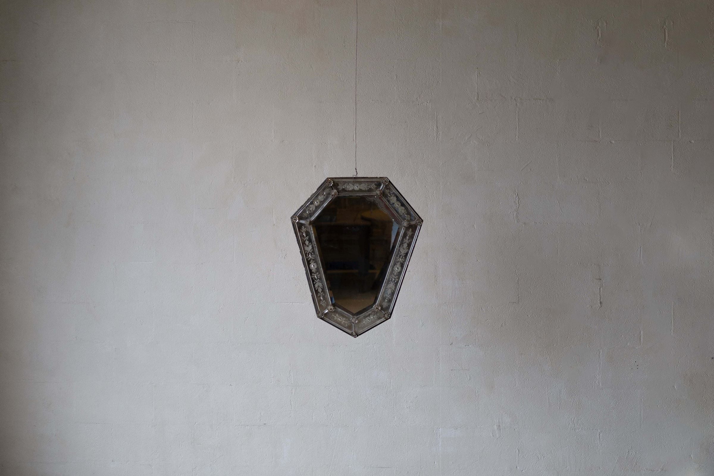 Wide image of Venetian crystal mirror with shield silhouette and bevelled glass frame against a white wall.