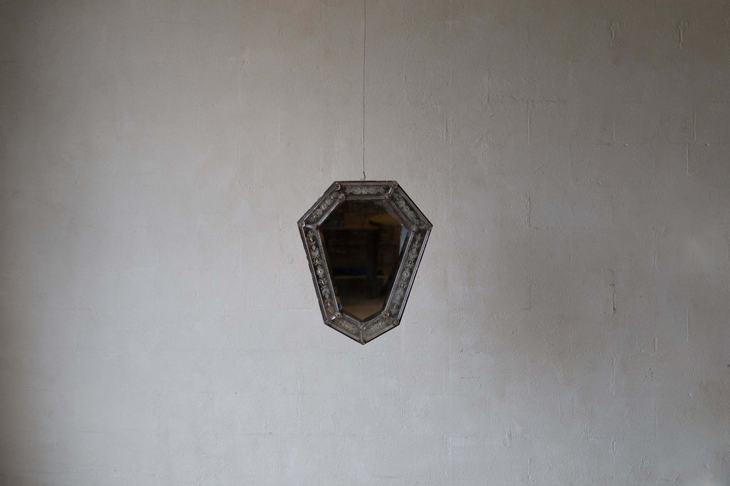 Wide image of Venetian crystal mirror with shield silhouette and bevelled glass frame against a white wall.