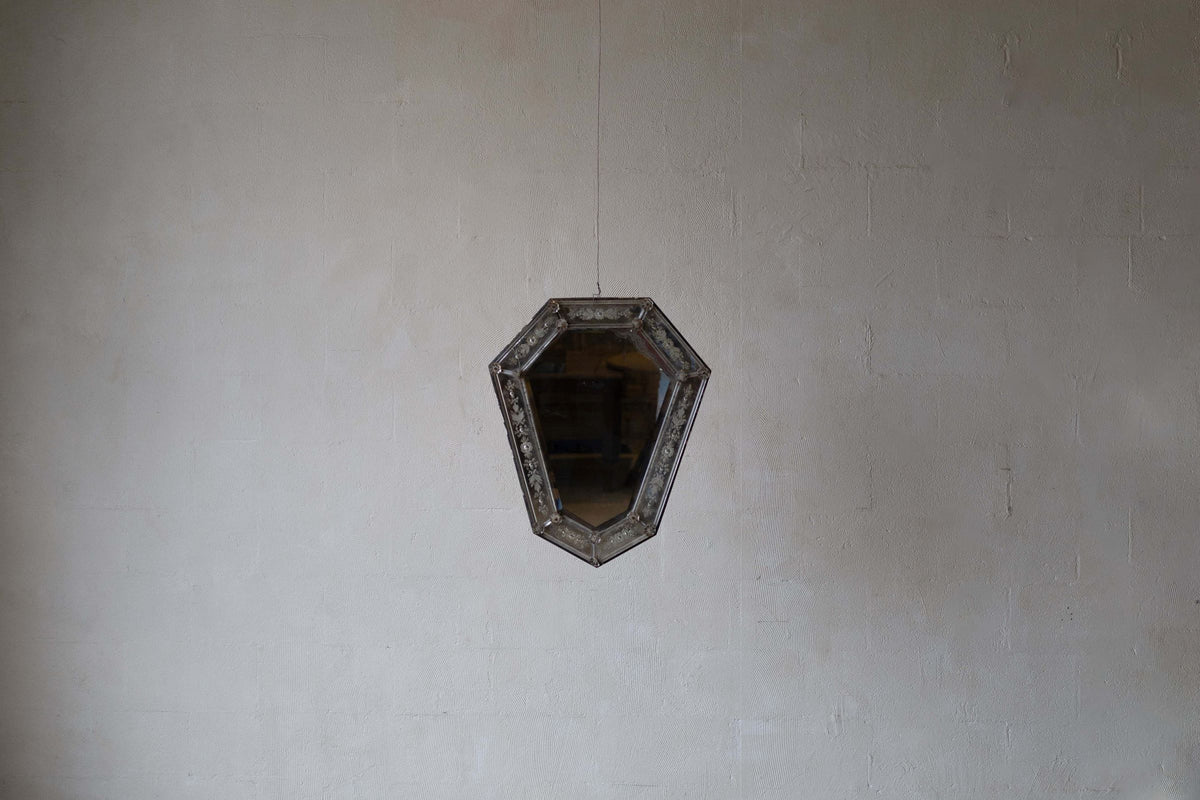 Wide image of Venetian crystal mirror with shield silhouette and bevelled glass frame against a white wall.
