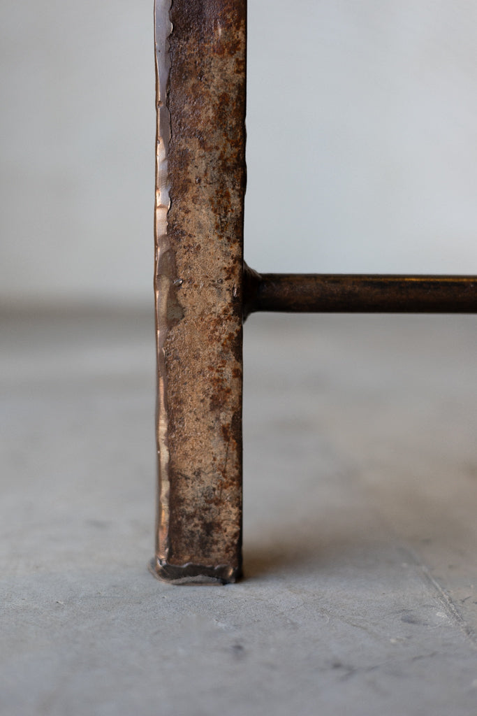 Close up of single leg of Vienna triangle table featuring rustic patina and welded of horizontal cross bar. 