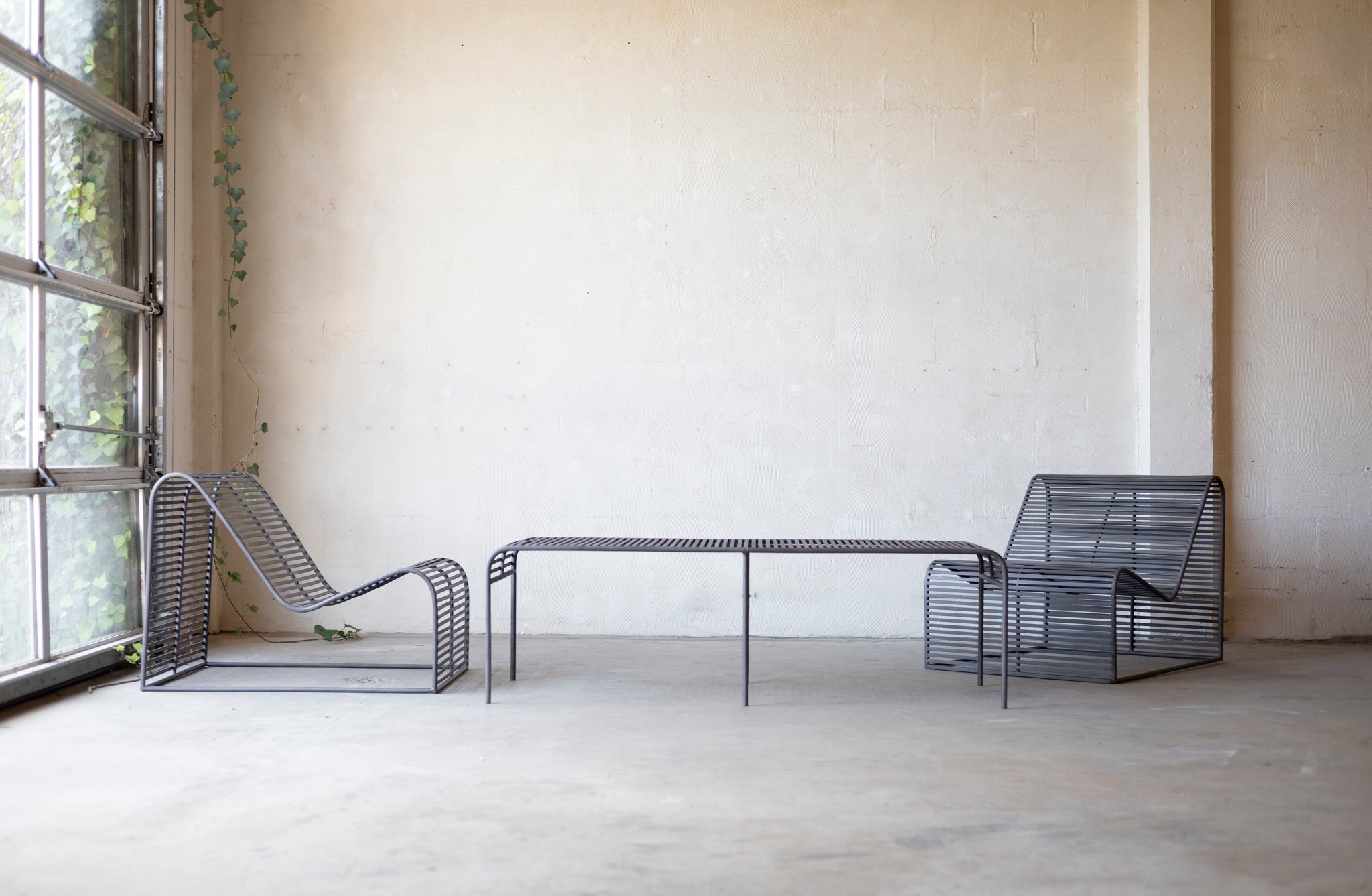 Modern wireframe chairs and table in a minimalistic room with large windows.