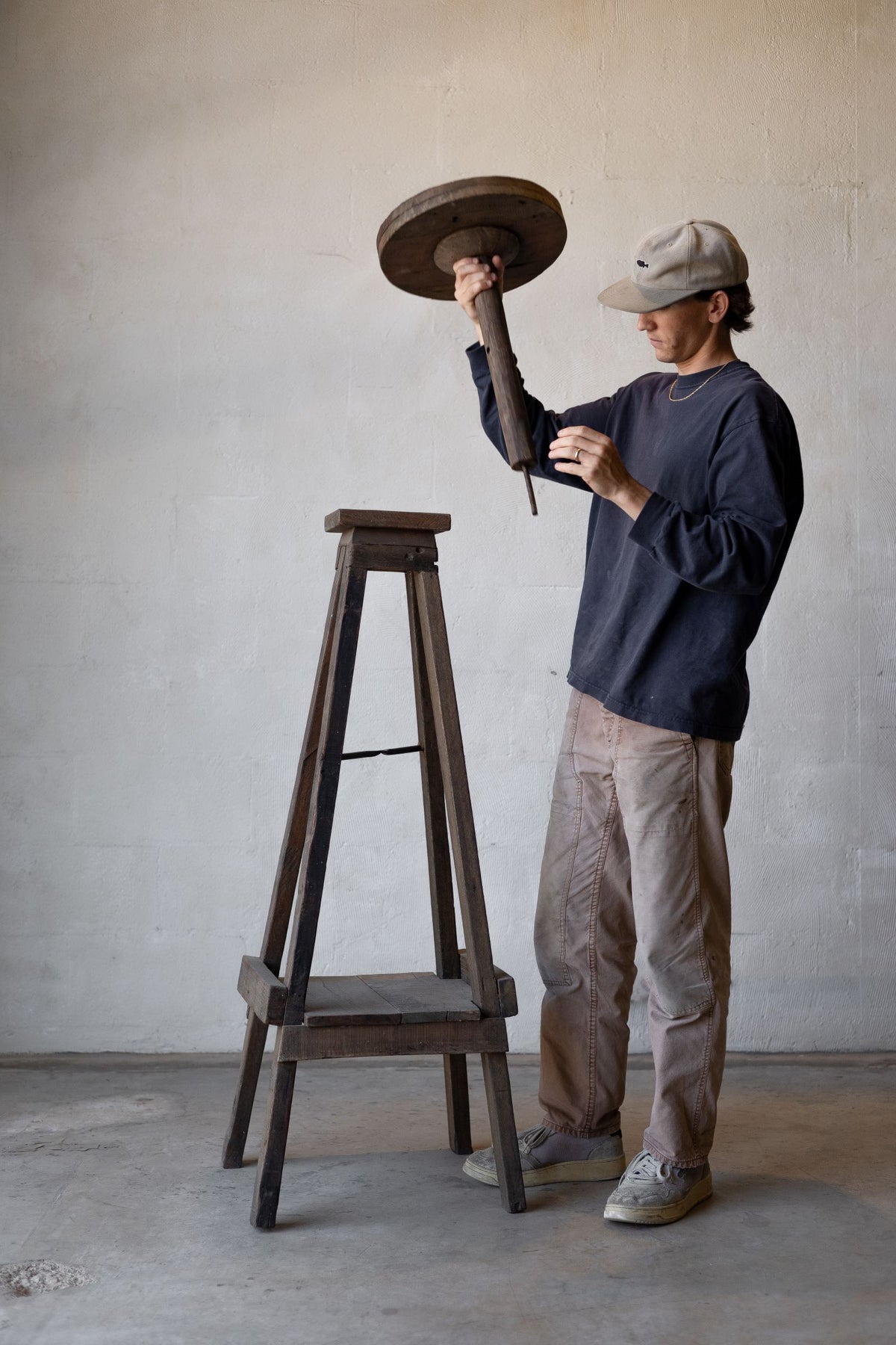 Reclaimed wood sculpture stand with man holding pedestal unattached from the stand. 