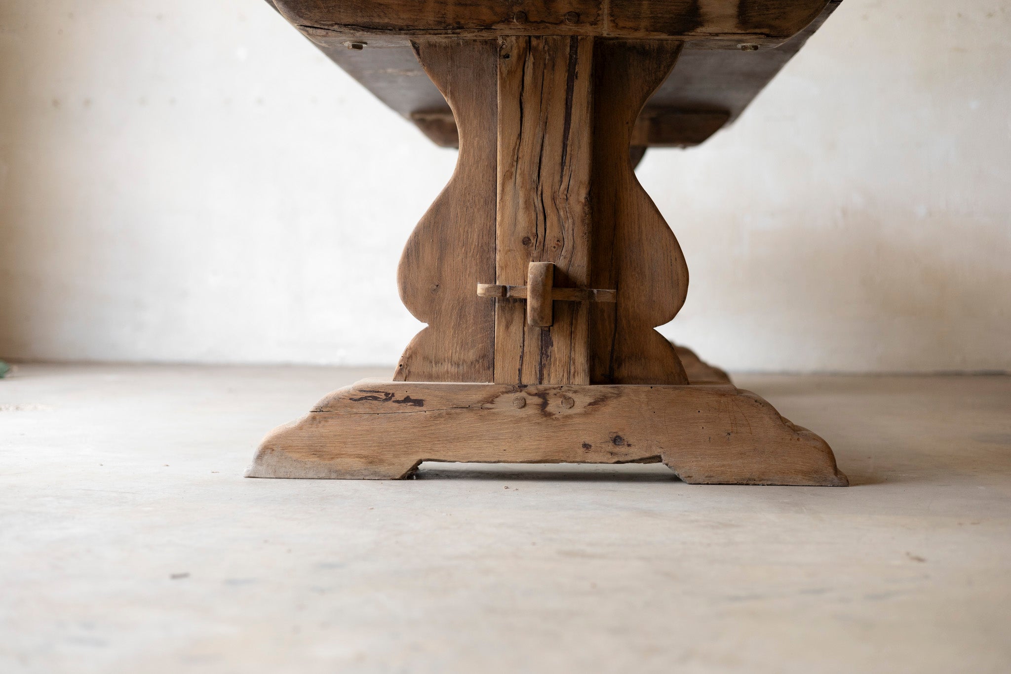 Wooden pedestal table base on a light wooden floor with a neutral background